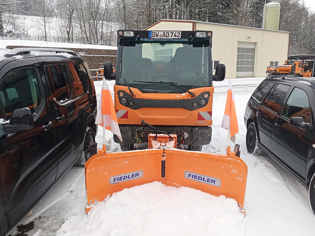 Fahrzeug mit Schneepflug zwischen zwei geparkten Autos